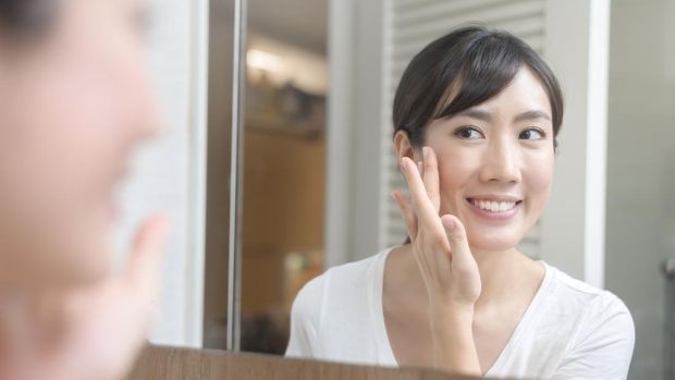 A happy beautiful woman applying moisturizing cream on face, skin care and treatment concept