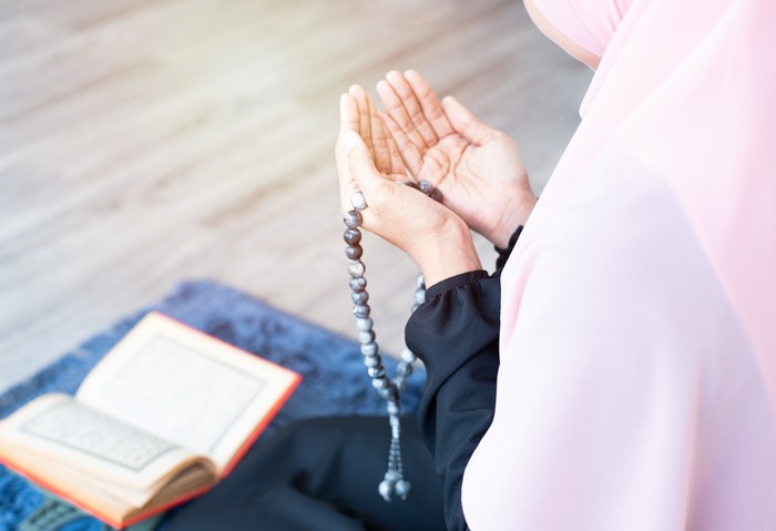 side of asian young beautiful muslim woman pray with beads and read quran sit on carpet mat with meditation in mosque.