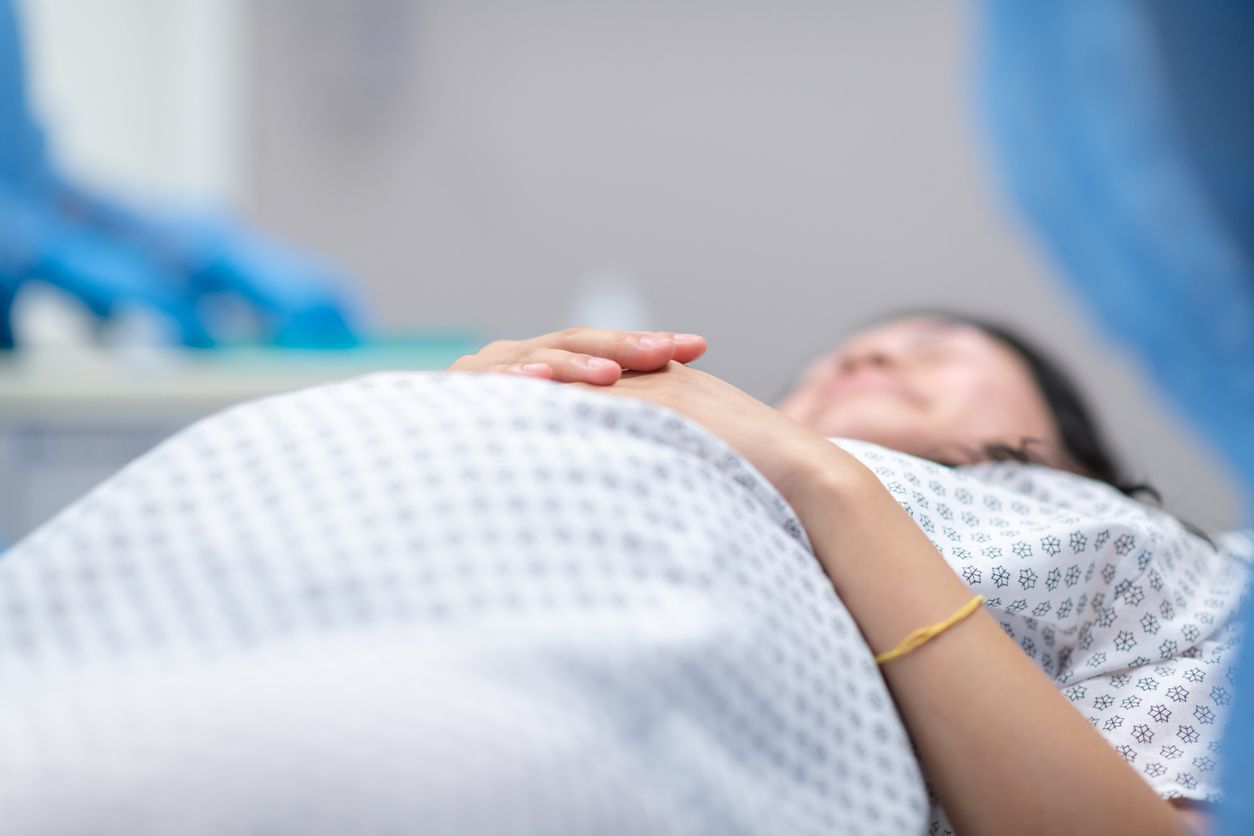 A pregnant woman is going in to surgery. She is laying on an operating table in the hospital's operating room. Surgeons surround the bed preparing for the medical procedure.