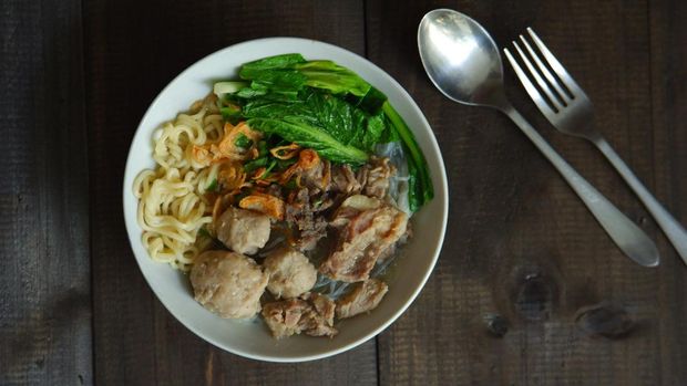 A bowl of meatball soup and vegetables in wooden background