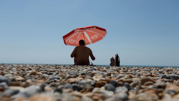 A man sits under an umbrella on Brighton beach, during a heatwave in Brighton, Britain, July 19, 2022. REUTERS/Peter Cziborra
