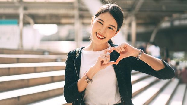Happy smile young adult asian business single woman hand up with heart gesture. Wear silver accessory and charm for lover faith on valentine day. City people lifestyle concept.