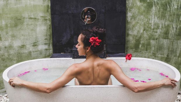 Woman relaxing in round outdoor bath with tropical flowers, organic skin care, luxury spa hotel, lifestyle photo