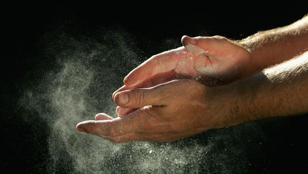 A sportsman chalks his hands in front of a black background