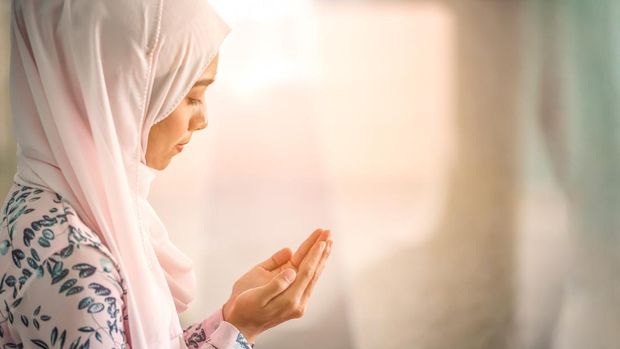 Young beautiful muslim women open palm, peaceful praying in mosque.