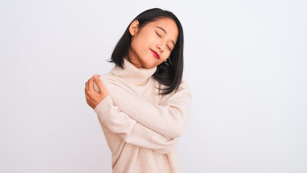 Young chinese woman wearing turtleneck sweater standing over isolated white background Hugging oneself happy and positive, smiling confident. Self love and self care