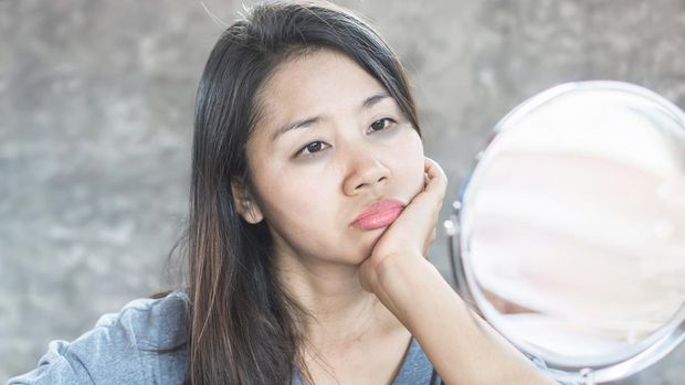 unhappy Asian woman age 40 checking her dark eyes circle problem in mirror