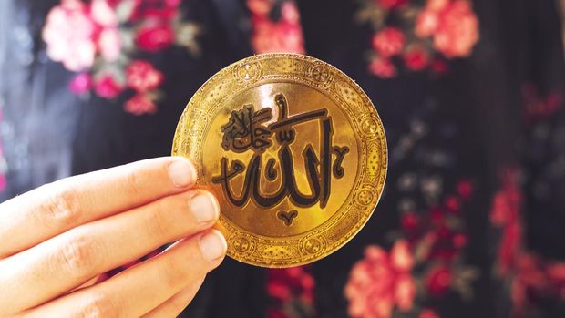 muslim woman holding a golden paper  with Arabic calligraphy of Allah (Islamic God)