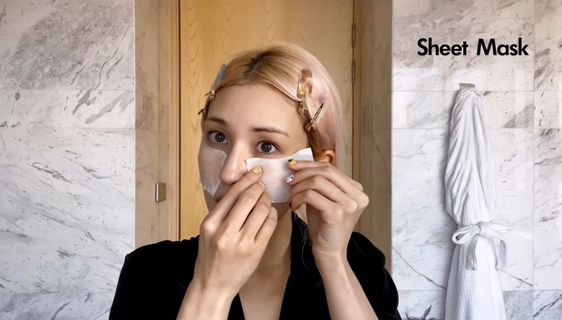 Langkah ketiga adalah mengaplikasikan Hyaluronic Acid Serum sebagai sheet mask/ Foto: Channel Youtube Vogue So Mi mengompres wajahnya dengan menggunakan kapas yang dituangi Hyaluronic Acid serum sebagai sheet mask