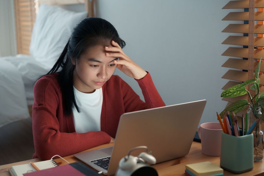 Asian girls are sitting stressed studying online with a tutor on a laptop while sitting in the bedroom at home night. Concept online learning at home