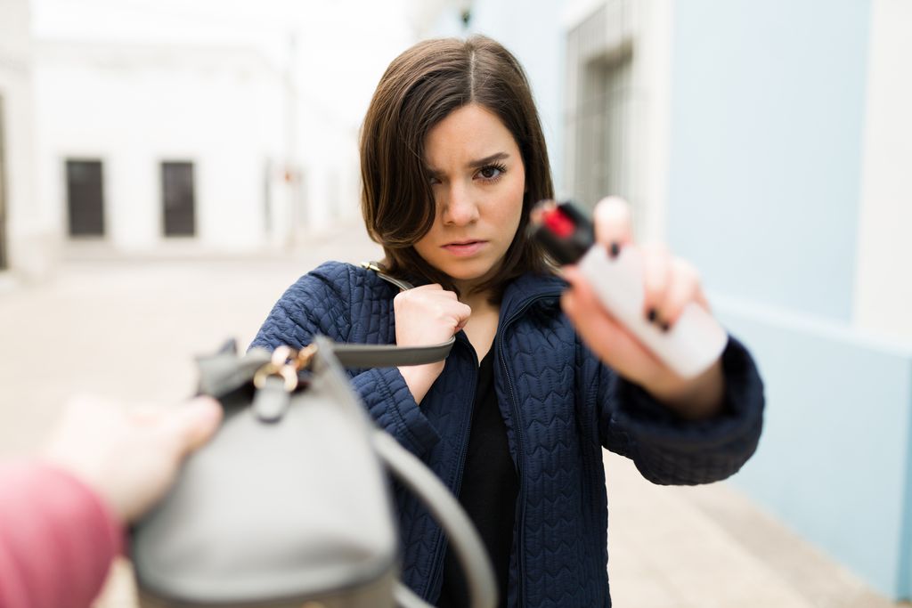 Angry caucasian woman using a pepper spray to defend herself from a robbery outdoors
