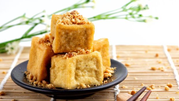 Fried tofu is stacked, sprinkled with peanuts on a black plate and chopsticks are placed on a wooden floor, food of vegetarian, popular food of vegetarian festival.