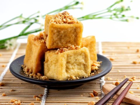 Fried tofu is stacked, sprinkled with peanuts on a black plate and chopsticks are placed on a wooden floor, food of vegetarian, popular food of vegetarian festival.