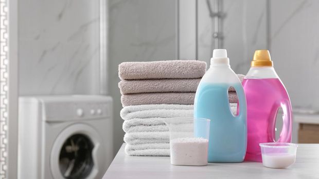 A stack of folded towels and laundry detergent on a white table in the bathroom