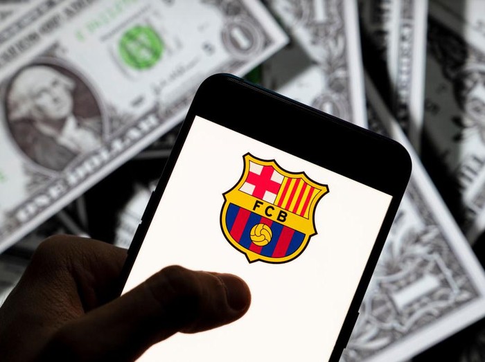 CHINA - 2021/04/23: In this photo illustration the Spanish professional football team the Futbol Club Barcelona logo seen displayed on a smartphone with USD (United States dollar) currency in the background. (Photo Illustration by Budrul Chukrut/SOPA Images/LightRocket via Getty Images)