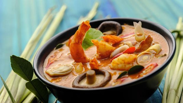 This Thai recipe known in Thai as 'Tom Yam Kungi' dish is very famous and known all over the world and one of Thailand's popular signature dishes when it comes to Thai food. This soup dish consists of ingredients including fresh prawns with fresh coconut milk, mushroom, galangal, shallots, lemongrass, kaffir lime leaves, and spicy fresh red chili. The combination of ingredients results in a spicy sour taste with a variety of complementary textures and is normally eaten together with fresh steamed Jasmine Thai rice. The image was taken from a high angle with the bowl set on a contrasting turquoise-colored wood-paneled table background.