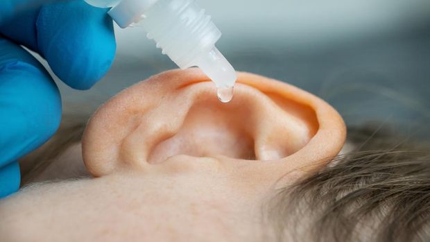 An otologist puts a drop in the patient's ear.  ear pain and blocked ears thought