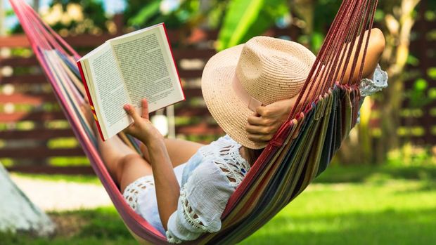 Woman reading book in hammock in tropical garden