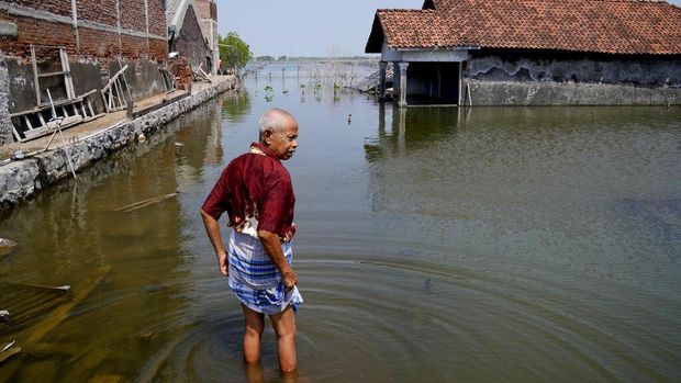 Sukarman walks on a flooded pathway outside his house in Timbulsloko, Central Java, Indonesia, Saturday, July 30, 2022. Sukarman thinks younger people, such as his granddaughter Dwi Ulfani, should try to move out of the village if they can. But he's resigned to the fact that with no money or other family homes, he's likely to spend the rest of his life living in an increasingly flooded home. (AP Photo/Dita Alangkara)