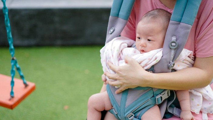 Close up Asian Baby girl inside  baby backpack with her mother sit in swing in playgrounds.