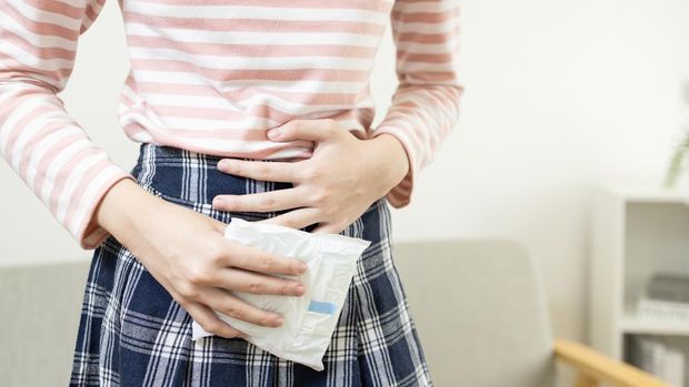 Teenage lady girl holding a sanitary napkin in hand,painful menstruation or abdominal cramps,asian student clutches stomach with severe menstrual pain on the day of her period,dysmenorrhea concept