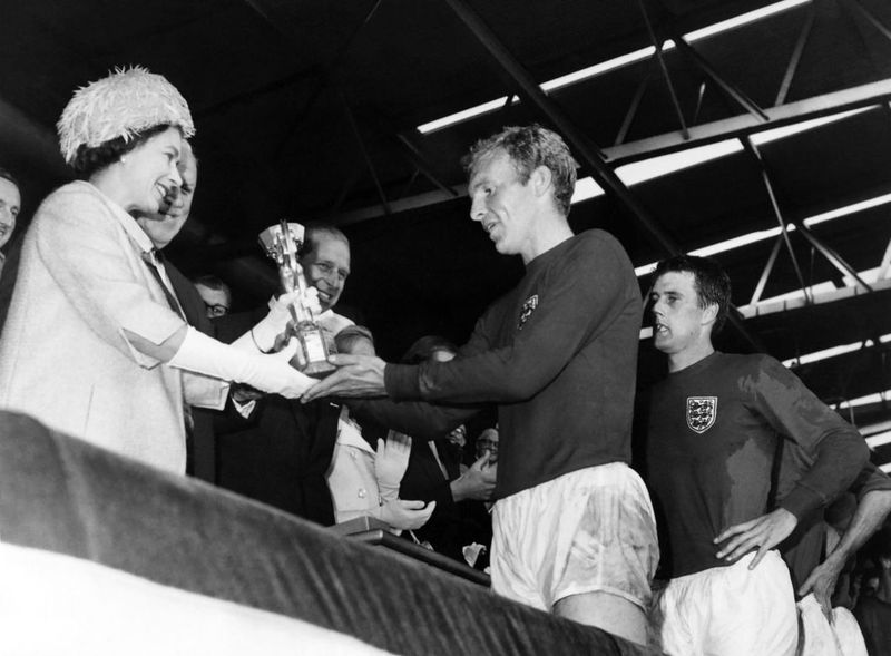 Piala Dunia 1966 Britain's Queen Elizabeth of England presents the Jules Rimet Cup to Bobby Moore, captain of England's national soccer team, as her husband Prince Philip (C) and forward Geoff Hurst (R) look on after England beat West Germany 4-2 in extra time in the World Cup final 30 July 1966 at Wembley stadium in London. - Hurst scored three goals, two of them in extra time, to help England win its first World title. (Photo by - / AFP) (Photo by -/AFP via Getty Images)