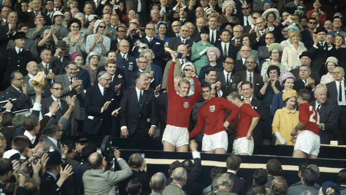 Piala Dunia 1966 Captain Bobby Moore holds the Jules Rimet trophy aloft following Englands 4 -2 victory against West Germany in the the World Cup Final at Wembley Stadium 30th July 1966. Geoff Hurst stands next to him and Roger Hunt is speaking to the Queen. (Photo by Fox Photos/Hulton Archive/Getty Images)