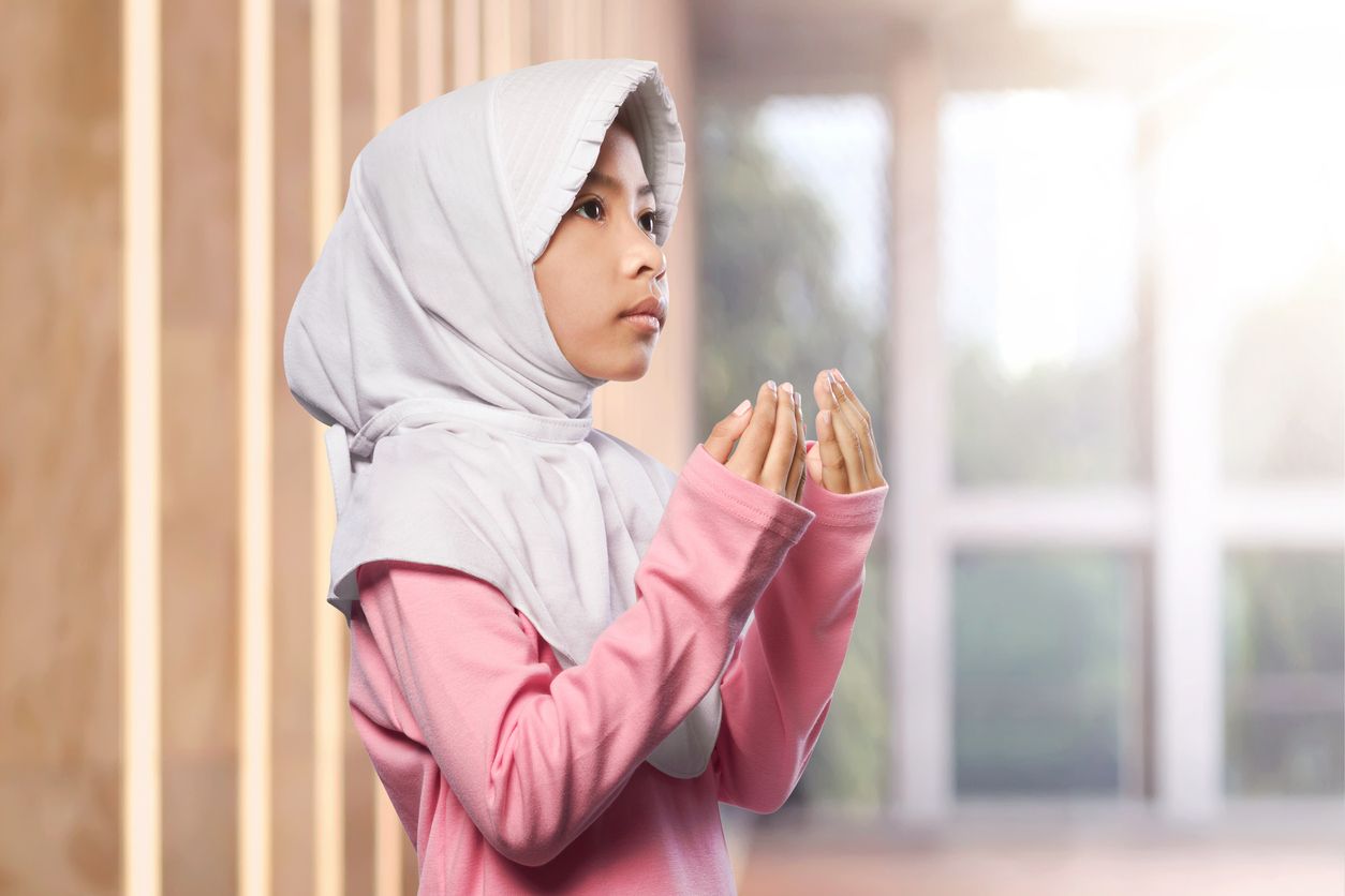 Portrait of asian muslim child raising hand and praying in the mosque