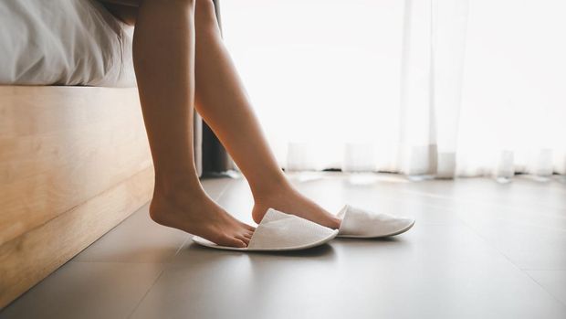 closeup woman legs with slippers sitting on bed