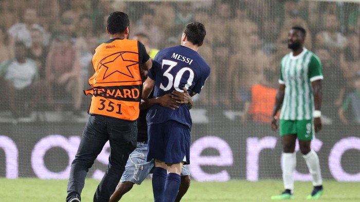 Detik-detik Fan Terobos Lapangan Demi Peluk Messi A steward interferes as a pitch invader hugs Paris Saint-Germain's Argentine forward Lionel Messi during the UEFA Champions League group H football match between Israel's Maccabi Haifa and France's Paris Saint-Germain (PSG) at the Sammy Ofer stadium in the city of Haifa on September 14, 2022. (Photo by RONALDO SCHEMIDT / AFP) (Photo by RONALDO SCHEMIDT/AFP via Getty Images)
