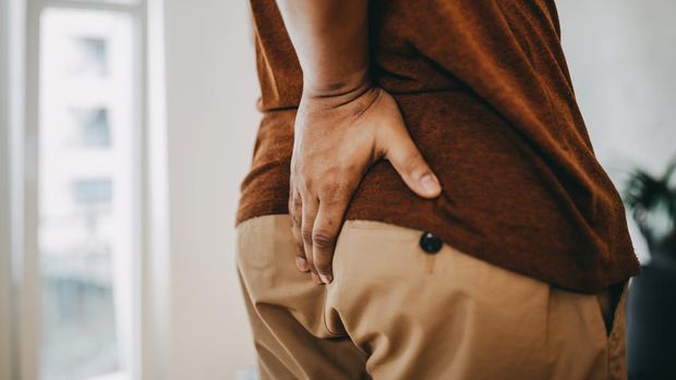 Man with hemorrhoids holding his butt in pain. Unrecognizable person with hemorrhoids and constipation. Man hand holding his bottom, having abdominal pain and hemorrhoids. Health care concept.