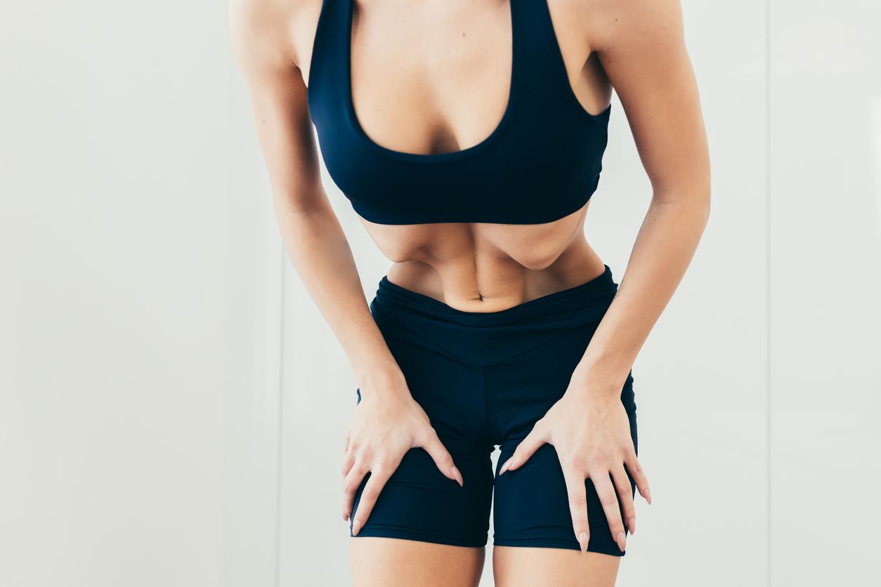 Vacuum for the abdomen pulling. Close up photo part of the body of a young beautiful sports woman standing and performing the exercise of pulling the abdomen in black sportswear