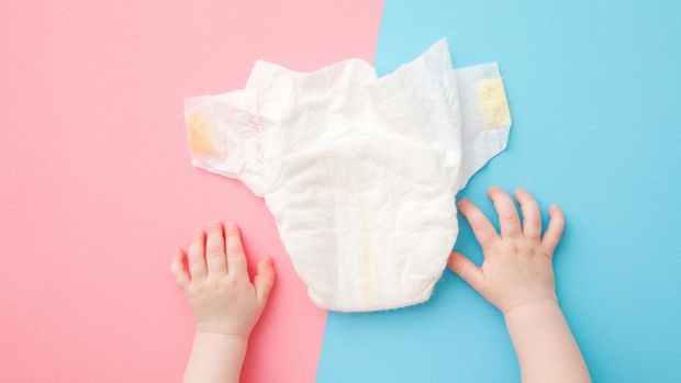 Baby hands and white diaper on light pink blue table background. Pastel color. Closeup. Point of view shot. Top down view.