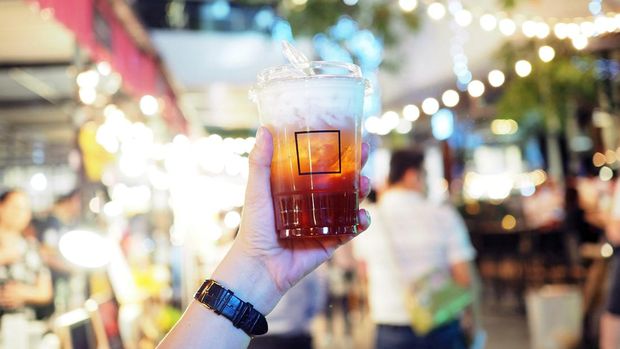 A plastic glass of iced black tea with layer of cream cheese foam. Trendy beverage. Selective focus. - ilustrasi es teh kekinian minuman manis