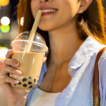 asian woman is holding bubble pearl milk tea outdoor in the evening