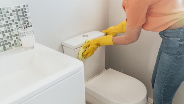 An unrecognizable mid-adult caucasian woman wearing protective yellow gloves is cleaning the toilet with a sponge in her bathroom at her home in Hartlepool.