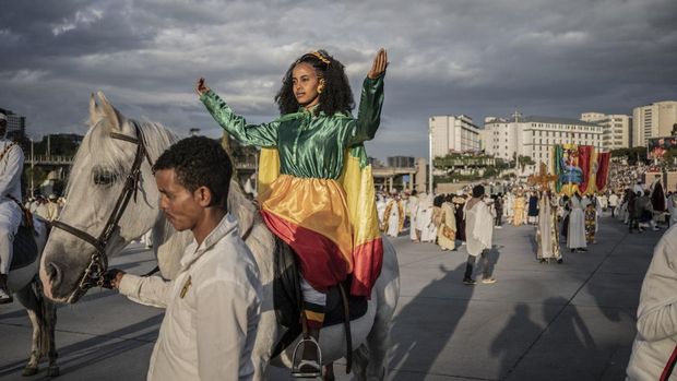 Festival Meskel di Ethiopia Rayakan Penemuan Salib Sejati A woman dressed with colors of Ethiopian flag raises her hand in a prayer during the celebrations in the eve of the Ethiopian Orthodox holiday of Meskel, in Addis Ababa on September 26, 2022. - The Ethiopia Meskel celebration is an annual religious holiday in the Ethiopian Orthodox church. It commemorates the supposed discovery in the fourth century by the Roman Empress Helena of the True Cross upon which Jesus was crucified. (Photo by Amanuel Sileshi / AFP)
