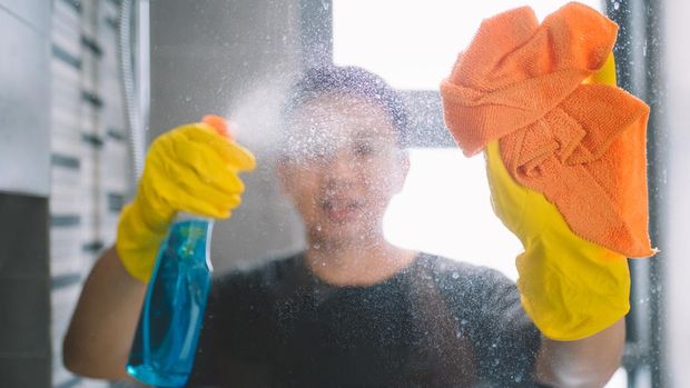 asian chinese male cleaning home with yellow gloves and orange colored cloth