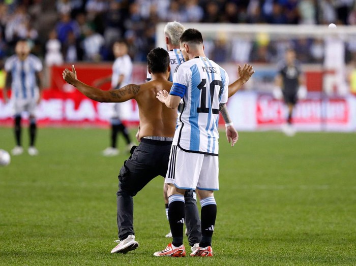 Argentina's Lionel Messi (R) signs an autograph for a fan who ran onto the pitch during the international friendly football match between Argentina and Jamaica at Red Bull Arena in Harrison, New Jersey, on September 27, 2022. (Photo by Andres Kudacki / AFP) (Photo by ANDRES KUDACKI/AFP via Getty Images)