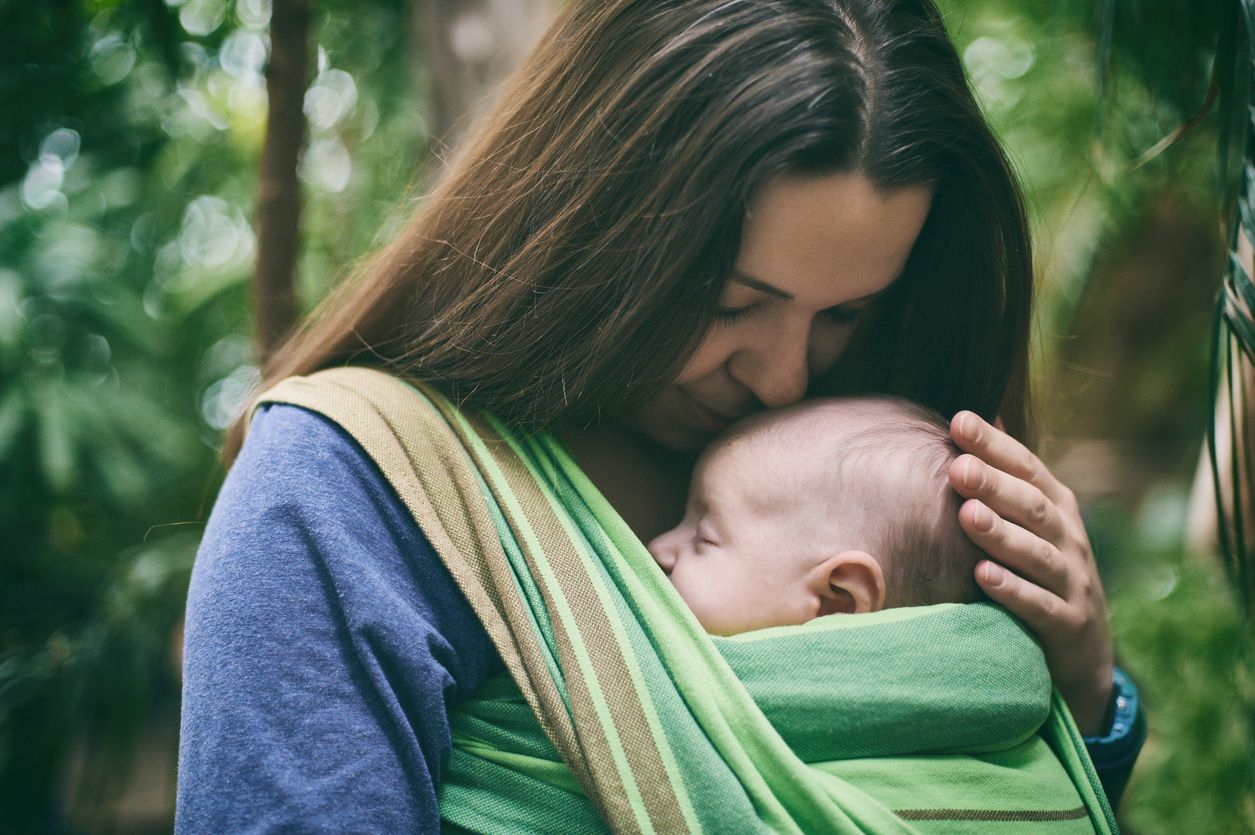A young mother with a baby in a sling is walking in the tropical forest