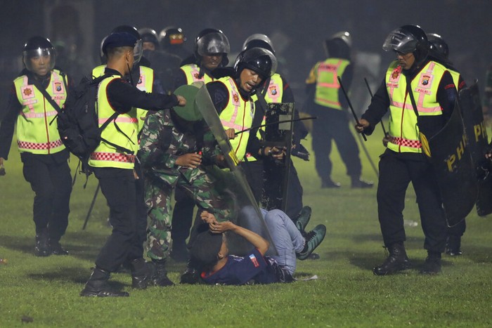 Police officers and soldiers stand amid tear gas smoke after clashes between fans during a soccer match at Kanjuruhan Stadium in Malang, East Java, Indonesia, Saturday, Oct. 1, 2022. Panic following police actions left over 100 dead, mostly trampled to death, police said Sunday. (AP Photo/Yudha Prabowo)