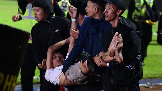 In this picture taken on October 1, 2022, a group of people carry a man after a football match between Arema FC and Persebaya Surabaya at Kanjuruhan stadium in Malang, East Java. - At least 127 people died at a football stadium in Indonesia late on October 1 when fans invaded the pitch and police responded with tear gas, triggering a stampede, officials said. (Photo by AFP)