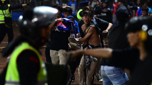In this picture taken on October 1, 2022, a group of people carry a man after a football match between Arema FC and Persebaya Surabaya at Kanjuruhan stadium in Malang, East Java. - At least 127 people died at a football stadium in Indonesia late on October 1 when fans invaded the pitch and police responded with tear gas, triggering a stampede, officials said. (Photo by AFP)