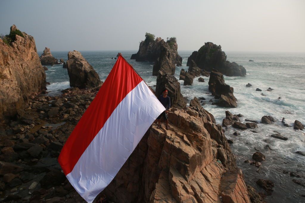 An Indonesian man seen carrying the Indonesian flag, on the rock of Tanggamus, Lampung, on August 16, 2019, in commemoration of the 74th Independence Day of the Republic of Indonesia. (Photo by: Ferdi Awed / INA Photo Agency /Universal Images Group via Getty Images)