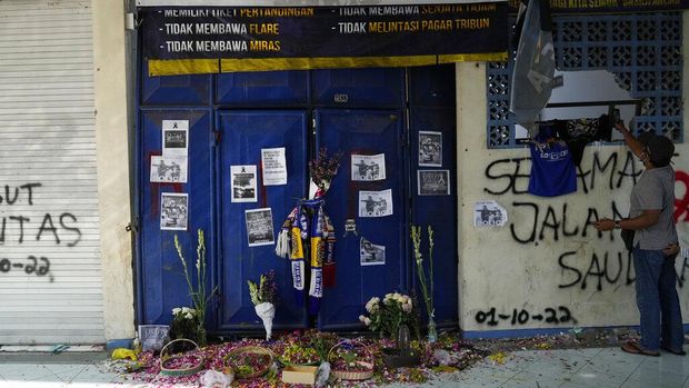People pray for victims of Saturday's soccer match stampede in front of gate 13 the Kanjuruhan Stadium in Malang, Indonesia, Tuesday, Oct. 4, 2022. Indonesian police said Tuesday that the gates at the soccer stadium where police fired tear gas and set off a deadly crush were too small and could only accommodate two at a time when hundreds were trying to escape. (AP Photo/Achmad Ibrahim)