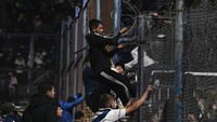 Penonton mulai panik, dan akhirnya memanjat pagar pembatas lapangan. Mereka menjebolnya untuk menjauh dari asap yang mengepul di tribune. (Foto: Gustavo Garello/Jam Media/Getty Images)