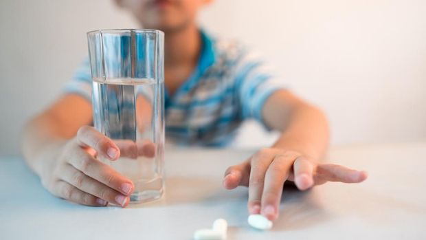 asian boy with cup of water and medicine in hand