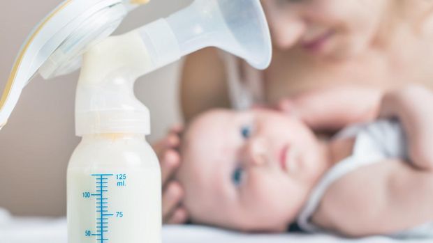 Manual breast pump and bottle with breast milk on the background of little baby in bed.