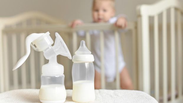 Manual breast pump and bottle with breast milk on the background of little baby in bed.