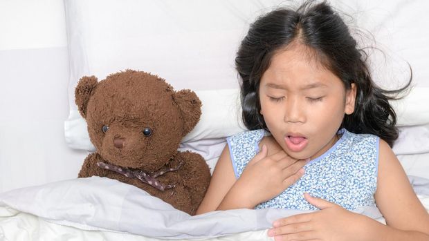 Little girl is coughing and sore throat lying on bed with toy bear, Health care concept
